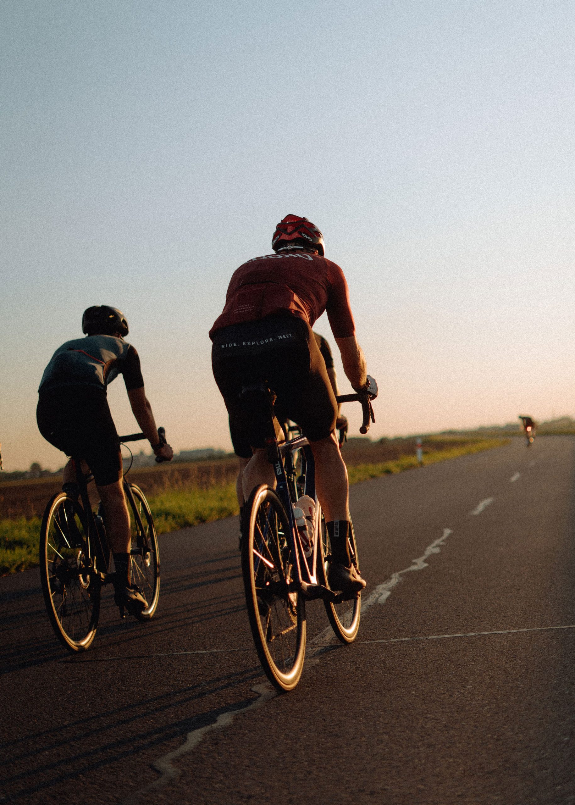 Two racing cyclists on a country road at sunset in the evening landscape.
